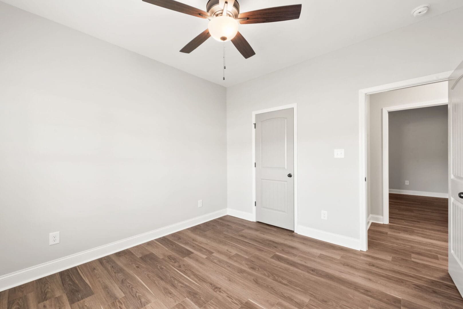 Empty bedroom with ceiling fan and wood floors.