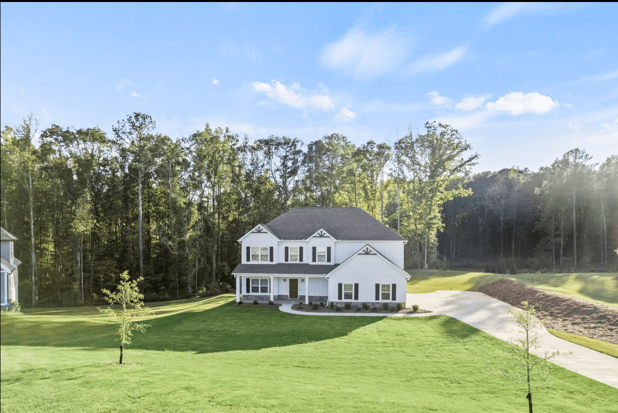 Two-story white farmhouse in wooded area.